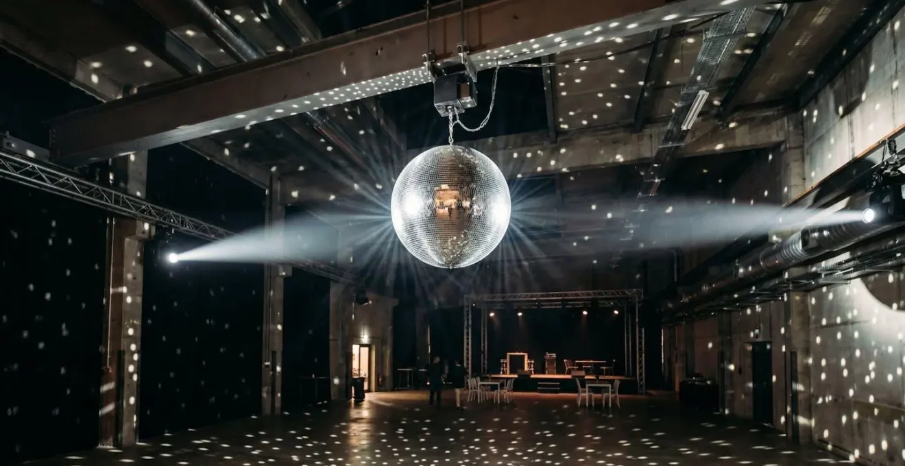 Boule à facettes motorisée suspendue au plafond d'une salle de fête, illuminée par des projecteurs créant des reflets lumineux scintillants