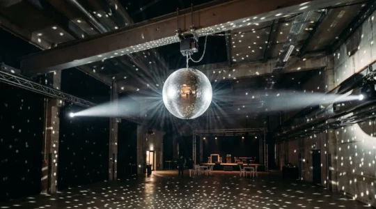 Boule à facettes motorisée suspendue au plafond d'une salle de fête, illuminée par des projecteurs créant des reflets lumineux scintillants